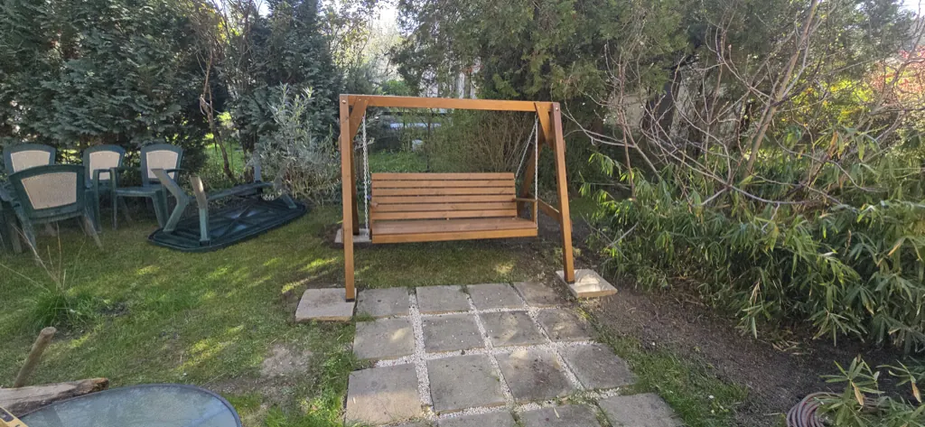 Fából készült kerti hinta kertben, kőlapos járda mellett